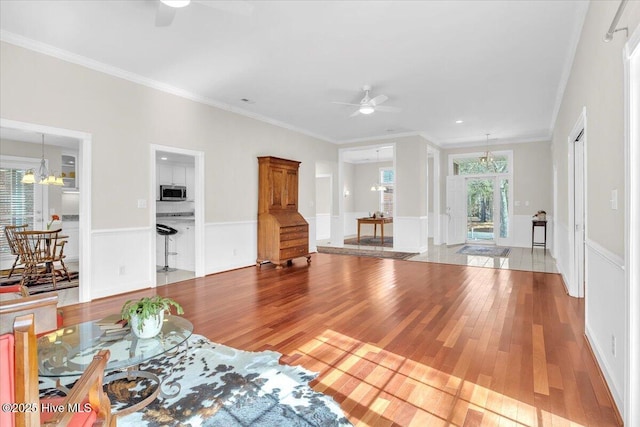 living room featuring ceiling fan with notable chandelier, wainscoting, wood finished floors, and crown molding