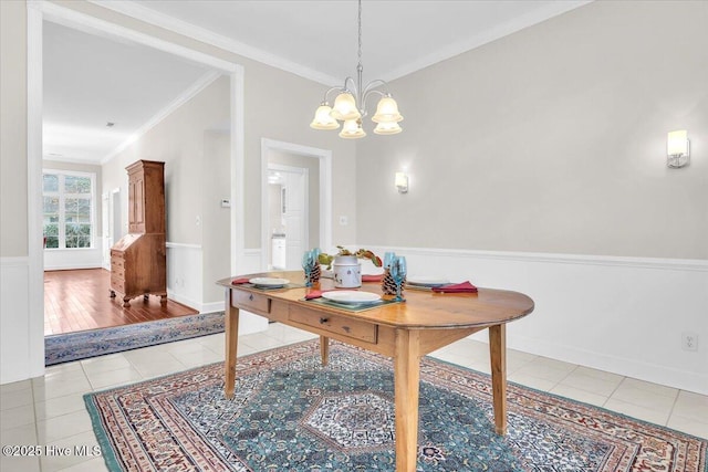 dining area with light tile patterned floors, ornamental molding, a chandelier, and wainscoting