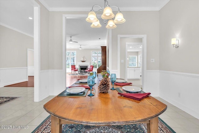 dining room with light tile patterned floors, ceiling fan with notable chandelier, a fireplace, baseboards, and crown molding