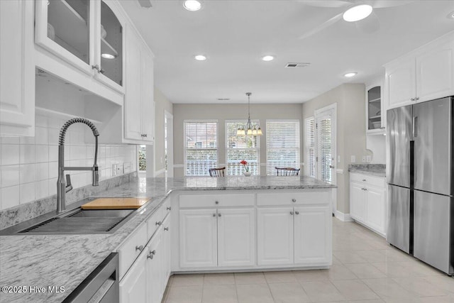 kitchen featuring stainless steel appliances, a peninsula, a sink, white cabinets, and backsplash