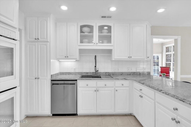 kitchen with light stone counters, white cabinetry, dishwasher, and a sink