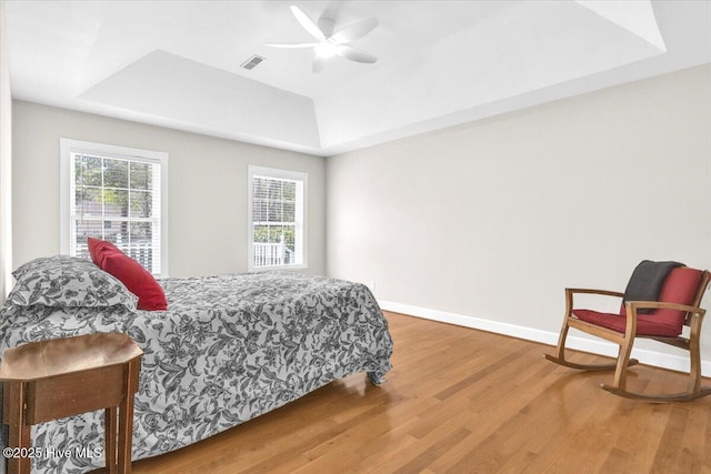 bedroom featuring a ceiling fan, baseboards, a tray ceiling, and wood finished floors