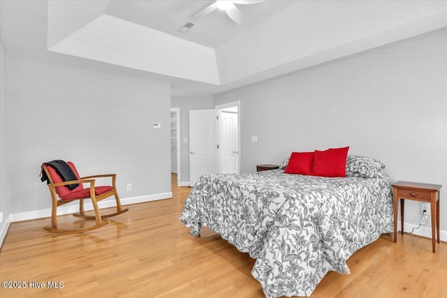 bedroom with light wood-style floors, a raised ceiling, visible vents, and baseboards