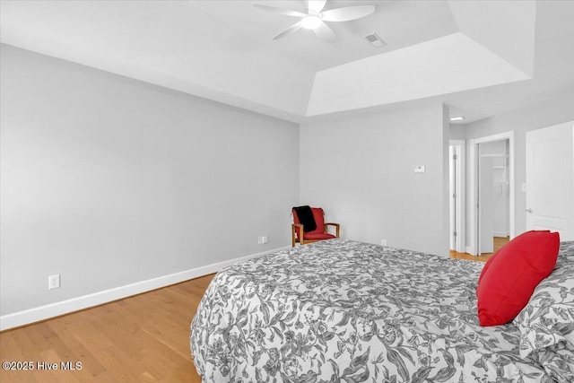 bedroom with wood finished floors, visible vents, a ceiling fan, baseboards, and a raised ceiling