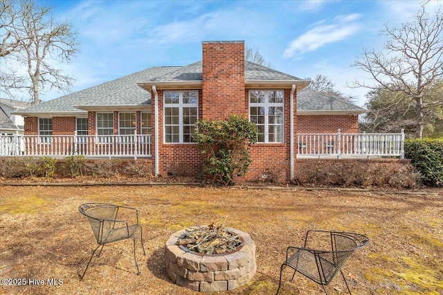 back of property with an outdoor fire pit, a chimney, roof with shingles, a porch, and brick siding