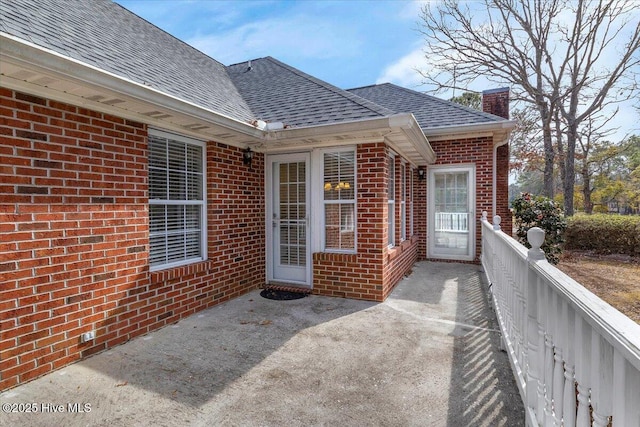 exterior space featuring a patio area, roof with shingles, a chimney, and brick siding