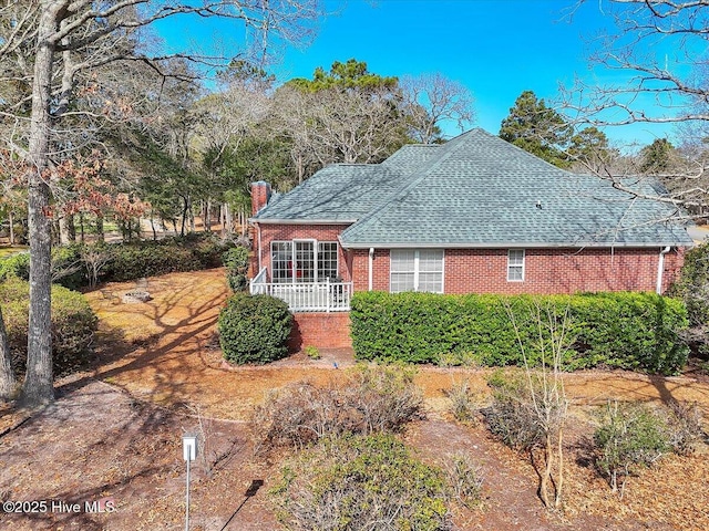 view of front facade with a shingled roof, a chimney, a porch, and brick siding