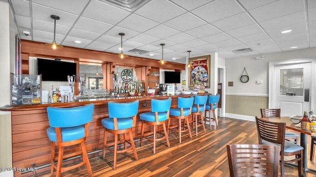 bar featuring a paneled ceiling, wainscoting, wood finished floors, and a community bar