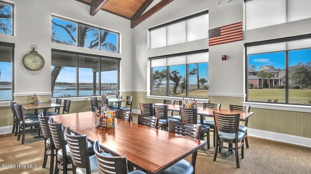 dining room featuring a wainscoted wall, a water view, high vaulted ceiling, wooden ceiling, and beamed ceiling