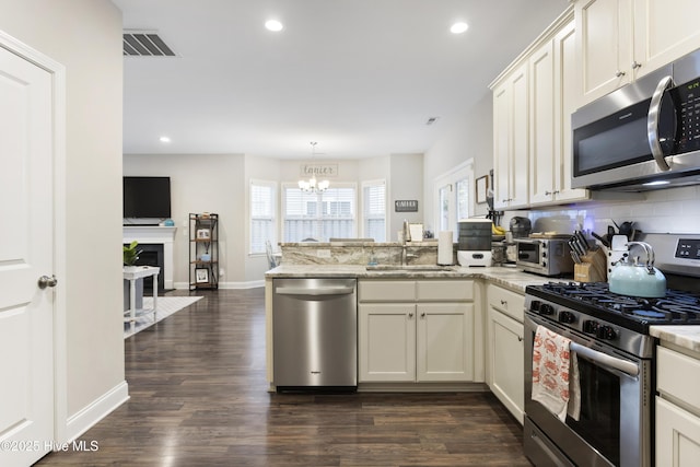 kitchen with stainless steel appliances, a peninsula, a sink, visible vents, and backsplash