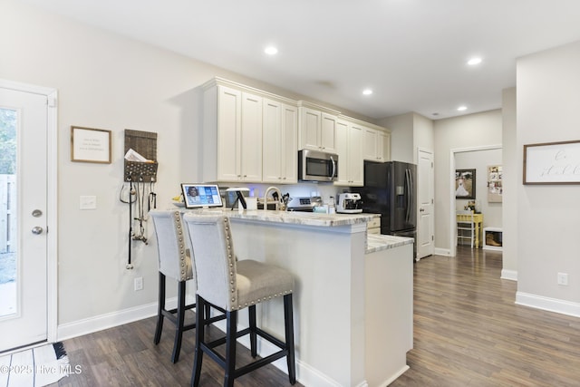 kitchen with dark wood-style floors, stainless steel microwave, a breakfast bar, a peninsula, and black fridge