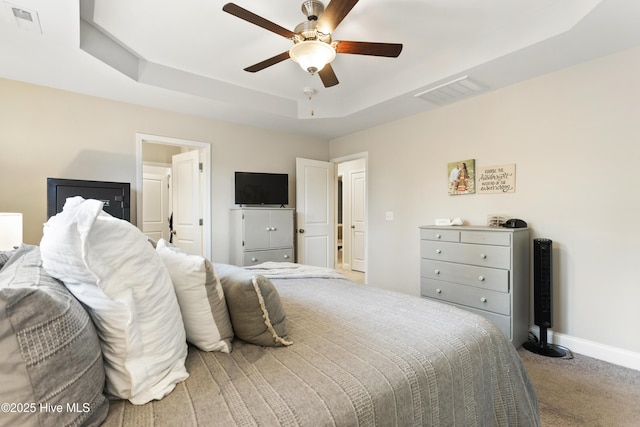 carpeted bedroom featuring ceiling fan, a raised ceiling, visible vents, and baseboards