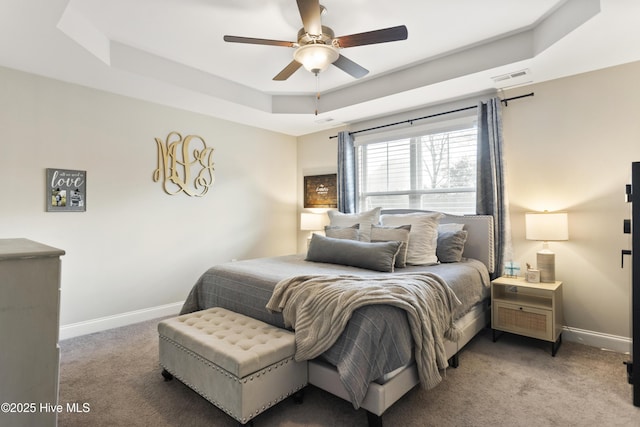 bedroom featuring carpet floors, a tray ceiling, visible vents, ceiling fan, and baseboards