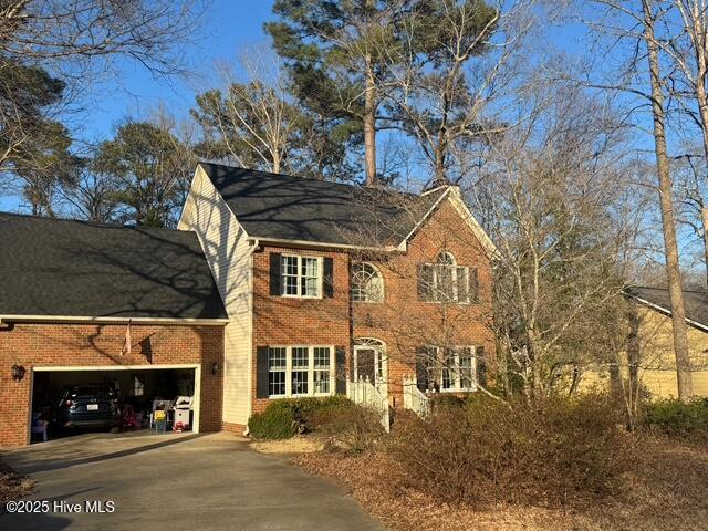 colonial house featuring brick siding, driveway, and an attached garage