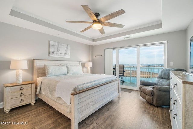 bedroom with dark wood-style floors, crown molding, a raised ceiling, and access to exterior