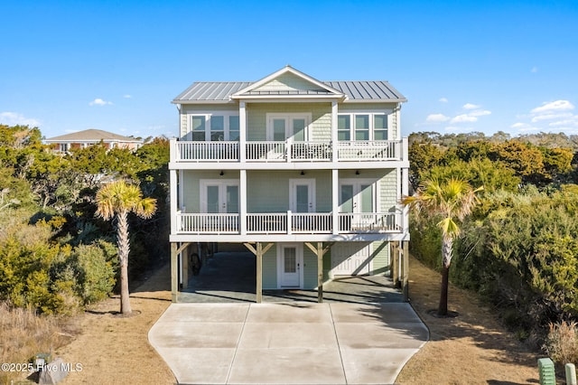 view of front of home with a balcony, a carport, concrete driveway, french doors, and metal roof