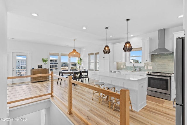 kitchen featuring a sink, stainless steel appliances, light countertops, white cabinets, and wall chimney exhaust hood