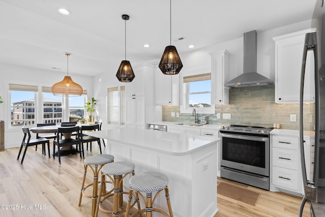 kitchen featuring a sink, light countertops, stainless steel range with electric stovetop, wall chimney exhaust hood, and backsplash