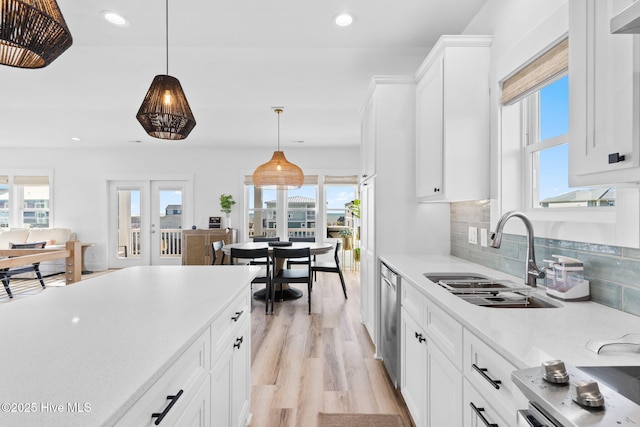 kitchen featuring white cabinetry, a sink, stainless steel dishwasher, light wood-type flooring, and backsplash