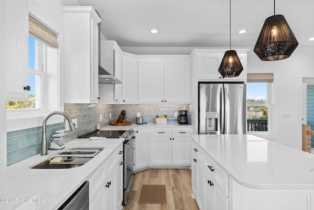 kitchen with light wood-style flooring, a sink, tasteful backsplash, appliances with stainless steel finishes, and wall chimney range hood