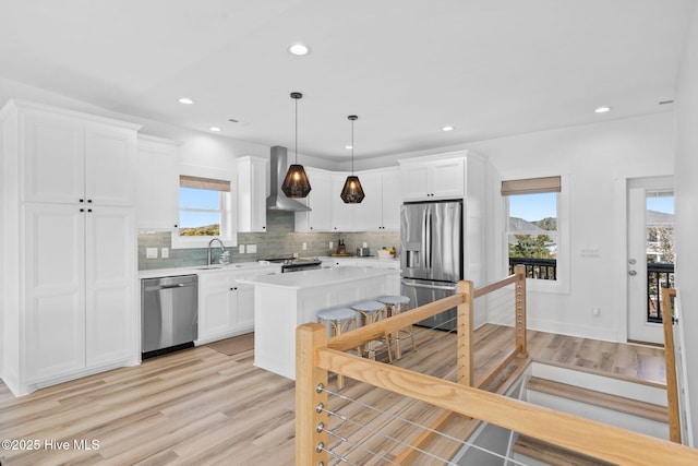 kitchen with light wood-type flooring, appliances with stainless steel finishes, light countertops, and wall chimney exhaust hood