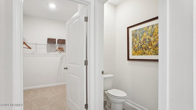 bathroom featuring a walk in closet, toilet, and baseboards