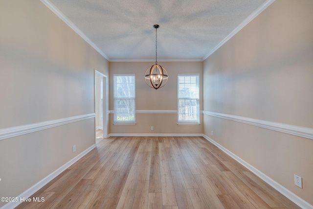 spare room featuring light wood-style floors, crown molding, baseboards, and a notable chandelier