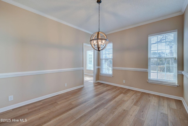 empty room featuring a chandelier, a wealth of natural light, crown molding, and light wood-style flooring