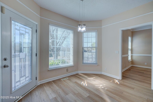 unfurnished dining area with a textured ceiling, baseboards, visible vents, and light wood-style floors