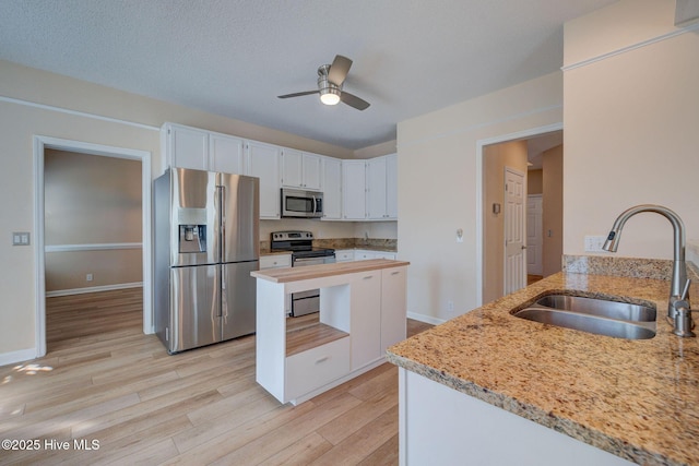 kitchen with light stone counters, stainless steel appliances, light wood-style floors, white cabinetry, and a sink