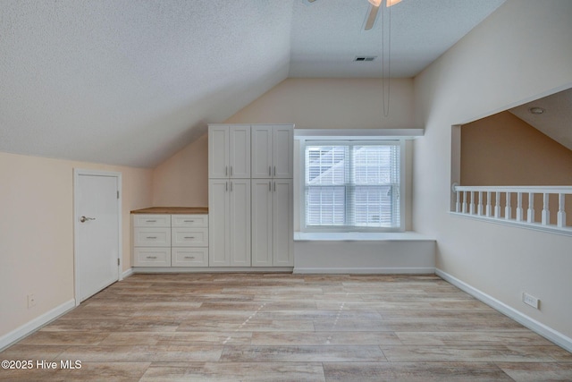 additional living space with visible vents, light wood-style flooring, a ceiling fan, vaulted ceiling, and a textured ceiling