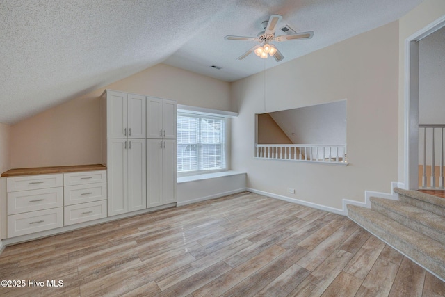 additional living space featuring lofted ceiling, a textured ceiling, light wood-style flooring, visible vents, and baseboards