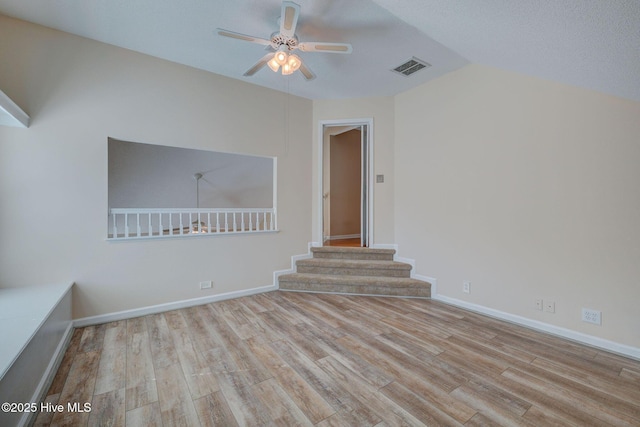 unfurnished room featuring baseboards, visible vents, a ceiling fan, wood finished floors, and stairs