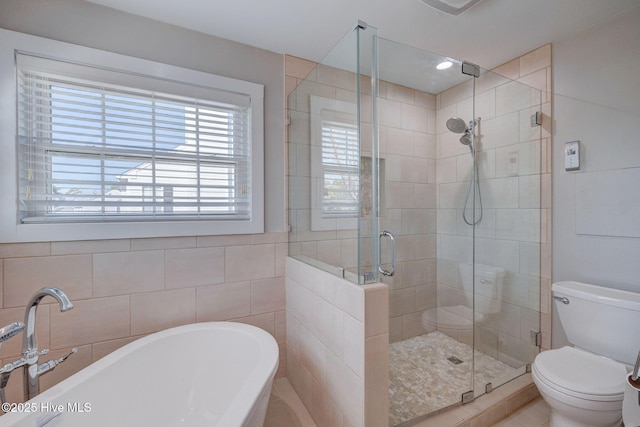 full bath featuring toilet, a soaking tub, tile walls, and a stall shower