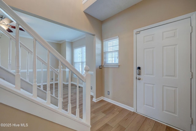 foyer with ceiling fan, baseboards, ornamental molding, stairway, and light wood-type flooring