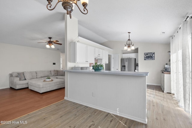 kitchen with stainless steel fridge, a peninsula, light countertops, light wood-style floors, and white cabinetry