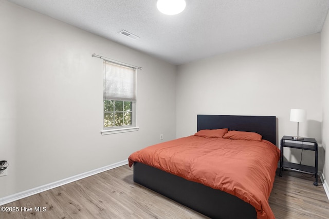 bedroom featuring visible vents, a textured ceiling, baseboards, and wood finished floors