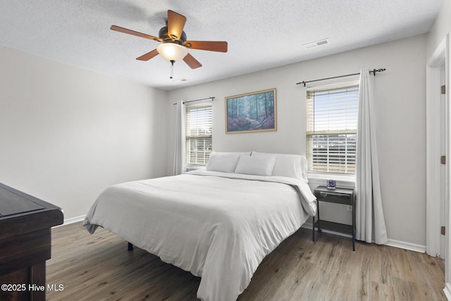 bedroom with visible vents, a textured ceiling, baseboards, and wood finished floors