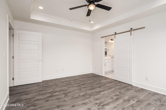 unfurnished bedroom with a tray ceiling, a barn door, wood finished floors, and crown molding