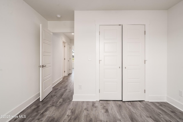 unfurnished bedroom featuring dark wood-style floors, a closet, and baseboards