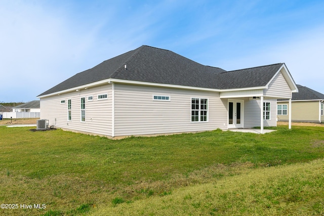 rear view of house featuring a patio, central AC unit, a shingled roof, french doors, and a lawn