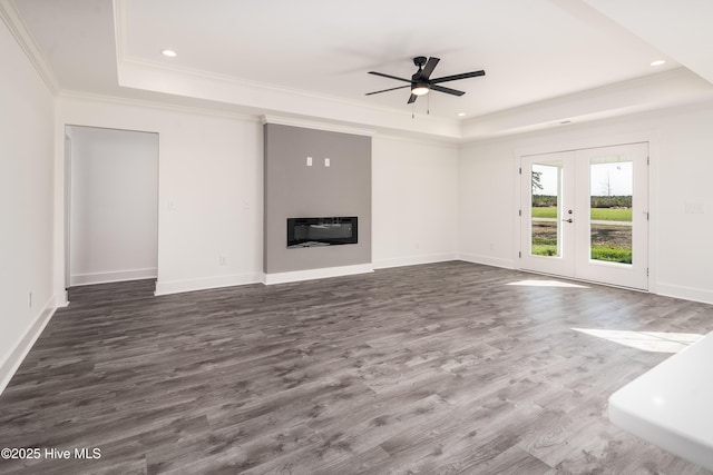 unfurnished living room featuring a glass covered fireplace, a raised ceiling, dark wood-type flooring, and ornamental molding