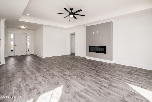 unfurnished living room featuring wood finished floors, baseboards, a tray ceiling, ornamental molding, and a glass covered fireplace