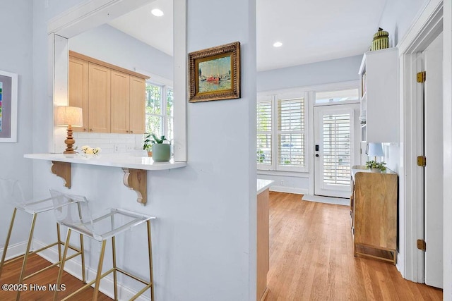 kitchen with tasteful backsplash, a kitchen breakfast bar, light countertops, light wood-type flooring, and recessed lighting