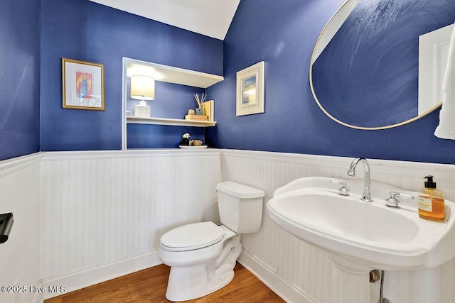 half bath with toilet, wood finished floors, a sink, and wainscoting