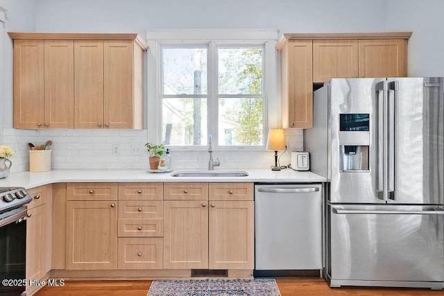 kitchen featuring light countertops, stainless steel appliances, a sink, and light brown cabinetry