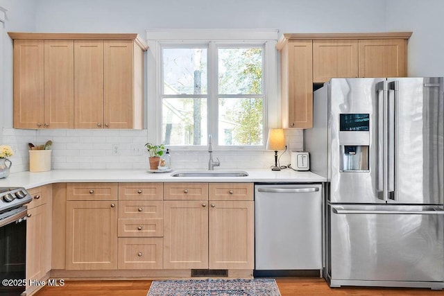 kitchen with light brown cabinetry, appliances with stainless steel finishes, a sink, light countertops, and decorative backsplash