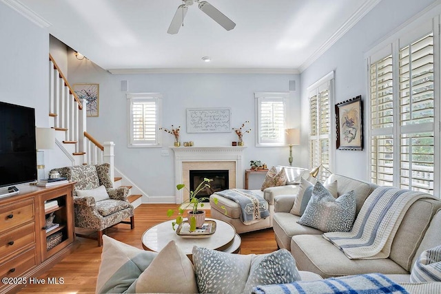 living area featuring ornamental molding, a glass covered fireplace, wood finished floors, baseboards, and stairs