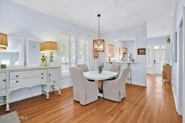 dining space with light wood-style floors, baseboards, ornamental molding, and a notable chandelier