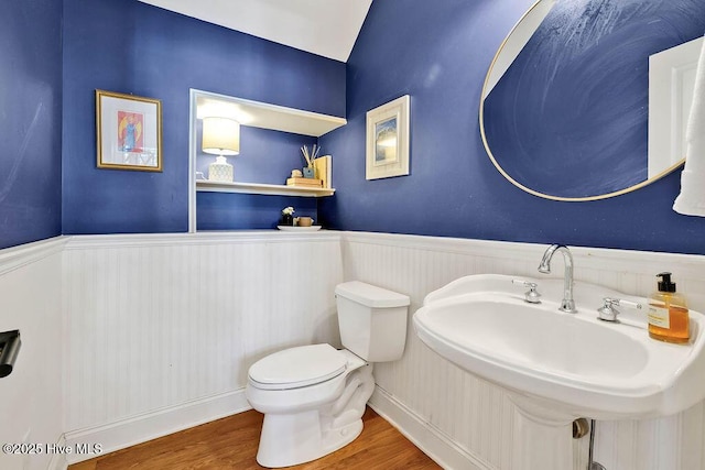 half bath featuring a sink, wainscoting, wood finished floors, and toilet